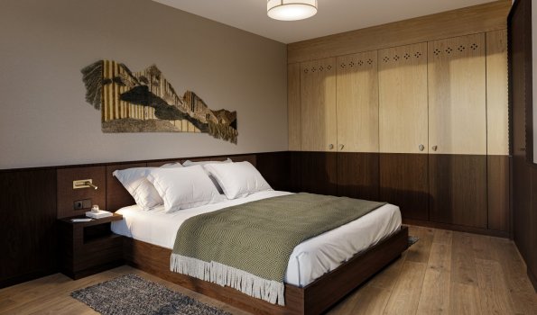 Schlafzimmer mit Holzverkleidung und einfacher Dekoration Im Schlafzimmer gibt es ein großes Bett mit weißen Kissen. Holzschränke und ein Teppich liegen auf dem Boden.
