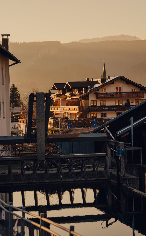 Blick auf die Häuser und Berge am Abend Die Sonne geht unter und beleuchtet die Gebäude in der Stadt. Das Wasser spiegelt die Farben des Himmels.