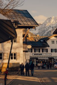Eine Gruppe von Menschen bewegt sich durch ein Dorf. Die Berge sind im Hintergrund sichtbar und es ist Nachmittag.