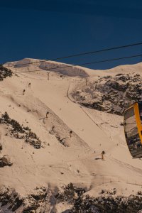 Eine Seilbahn transportiert Skifahrer über eine schneebedeckte Piste in den Bergen. Es ist sonnig und die Leute genießen die Abfahrt.