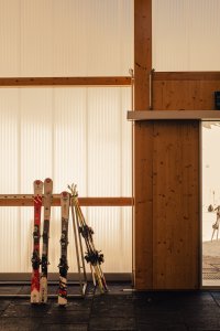 Die Ausrüstung steht an der Wand in einem Raum mit Tageslicht. Im Hintergrund sind Skier und Ständer sichtbar.