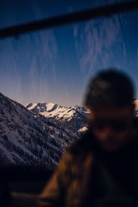 Eine Person sitzt in einer Gondel und schaut auf die Berge. Oft gibt es Schnee auf den Gipfeln und blauen Himmel.