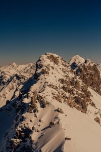 Ein Berggipfel mit Schnee und Felsen ist vor einem klaren Himmel zu sehen. Die Landschaft zeigt hohe, schneebedeckte Berge.