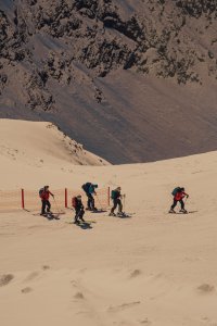Gruppen von Skifahrern gehen auf einem Schneehang in den Bergen. Es ist winterlich und die Landschaft ist schneebedeckt.