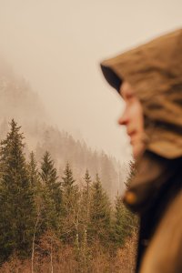 Ein Mann steht in der Nähe eines Waldes und schaut in die Ferne. Es ist neblig und die Bäume sind hoch.