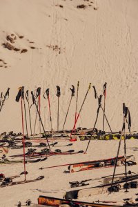Auf einer Schneepiste stehen viele Skier mit Skistöcken. Es ist tagsüber und der Schnee ist frisch.