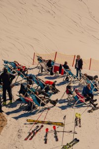Menschen sitzen auf langen Sesseln im Schnee und genießen die Sonne in den Bergen nach dem Skifahren.