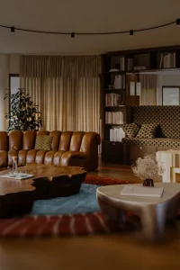 In einem großen Raum steht eine Ledercouch in U-Form. Ein Tisch aus Holz und viele Bücher sind im Regal.