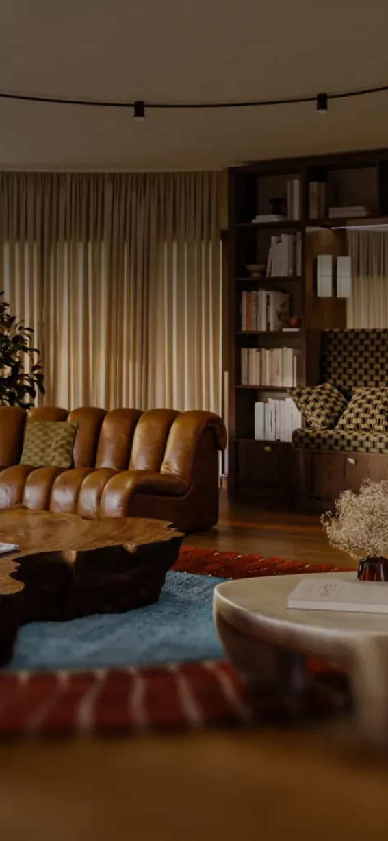 In einem großen Raum steht eine Ledercouch in U-Form. Ein Tisch aus Holz und viele Bücher sind im Regal.