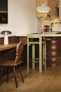 In einem modernen Raum stehen ein Tisch und Stühle in einer Küche. Die Wände sind hell und Holz ist sichtbar.