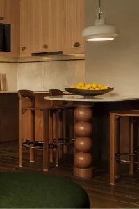 In der Küche stehen zwei Barstühle an der Theke. Auf dem Tisch ist eine Schale mit Äpfeln und Orangen.