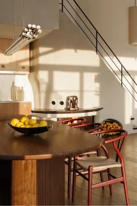 In einer modernen Küche stehen Schalen mit Zitronen und Orangen auf einem Tisch. Sonnenlicht fällt durch Fenster.