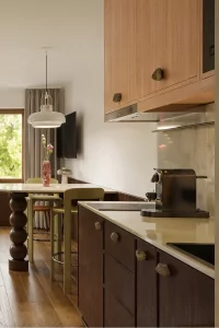 In einem Raum mit großen Fenstern ist eine moderne Küche zu sehen. Sie hat einen Tisch und eine Küchenzeile.