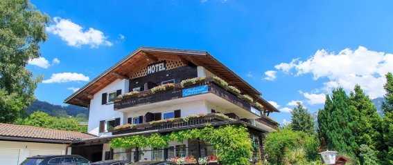 Hotel in einer ländlichen Umgebung mit Autos Das Hotel steht in einer ländlichen Umgebung. Es gibt viele Autos auf dem Parkplatz. Die Sonne scheint, der Himmel ist blau.