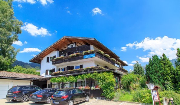 Hotel in einer ländlichen Umgebung mit Autos Das Hotel steht in einer ländlichen Umgebung. Es gibt viele Autos auf dem Parkplatz. Die Sonne scheint, der Himmel ist blau.