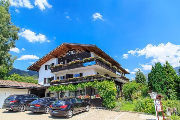 Hotel in einer ländlichen Umgebung mit Autos Das Hotel steht in einer ländlichen Umgebung. Es gibt viele Autos auf dem Parkplatz. Die Sonne scheint, der Himmel ist blau.