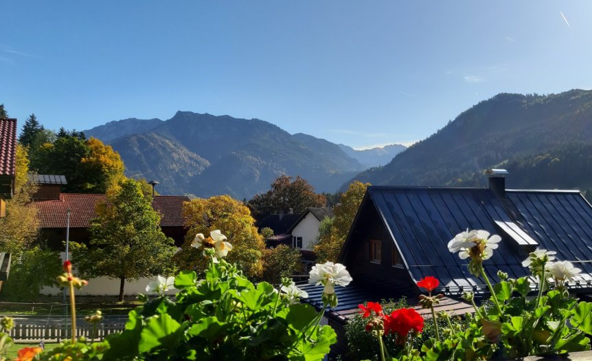Die Sonne scheint auf die Berge. Blumen und Häuser sind im Vordergrund sichtbar. Es ist ein klarer Tag in den Bergen.