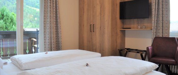 Doppelzimmer mit Blick auf die Berge In einem Zimmer mit zwei Betten sind die Fenster geöffnet. Das Zimmer zeigt den Blick auf die Berge und den Balkon.