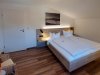 Doppelzimmer in einer Holzwohnung mit Schreibtisch In einem Zimmer befinden sich zwei Betten, ein Tisch und eine Lampe. Das Zimmer ist hell und hat eine Ablage.