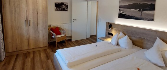 Das Zimmer hat zwei Betten, einen Schrank und einen Stuhl. Es ist hell und hat einen Zugang zur Tür.