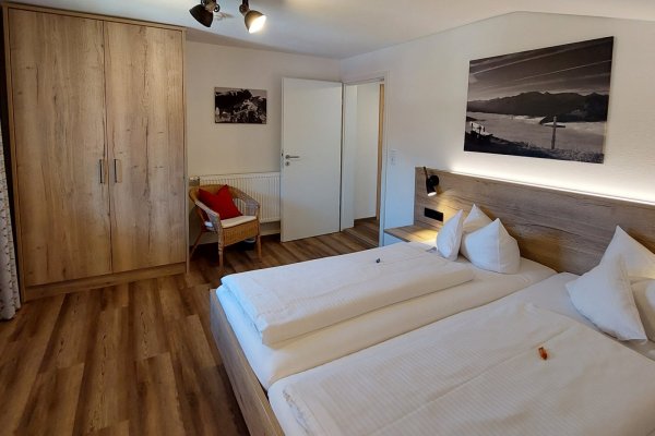 Zimmer mit zwei Betten in einer Unterkunft Das Zimmer hat zwei Betten, einen Schrank und einen Stuhl. Es ist hell und hat einen Zugang zur Tür.