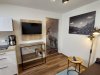 Moderne Einrichtung in einem Wohnzimmer In einem Wohnzimmer steht ein Fernseher an der Wand. Es gibt einen Tisch und einen Stuhl, sowie eine Küche in der Nähe.