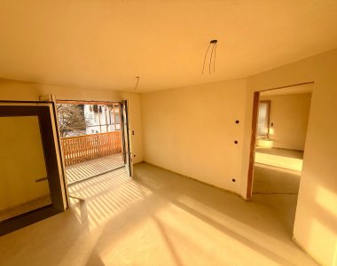 Der Raum hat große Fenster und führt zu einem Balkon. Es gibt keine Möbel und das Licht fällt auf den Boden.