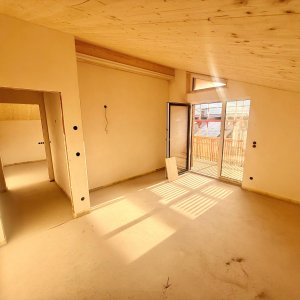 Das Zimmer zeigt eine leere Fläche mit Fenstern und einem Balkon. Der Raum wirkt hell und hat einen Holzfußboden. Neues Zimmer mit Zugang zum Balkon in einem Haus