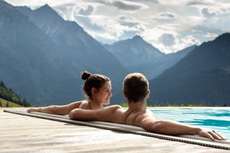 Ein Paar genießt die Aussicht vom Außenpool auf die Berge im Oberjoch - Familux Resort.