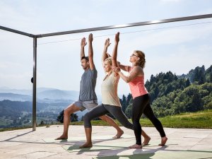 Ein Mitarbeiterin des Hotels Bergkristall - Mein Resort im Allgäu in Oberstaufen zeigt zwei Gästen eine Yoga Übung