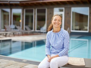 Mitarbeiterin im Hanusel Hof in Weitnau / Hellengerst sitzt auf einer Liege und dahinter ist der Außenpool zu sehen