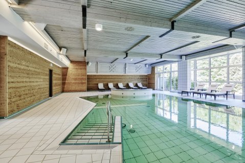 Eindruck vom Innenpool mit großen Fenstern und Liegen im Hotel Bannwaldsee in Halblech