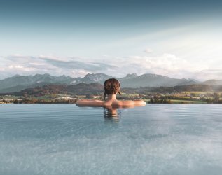 Eine Frau entspannt im Außenpool des Panorama Land- und Wellnesshotels in Rückholz und genießt dabei die wunderschöne Aussicht
