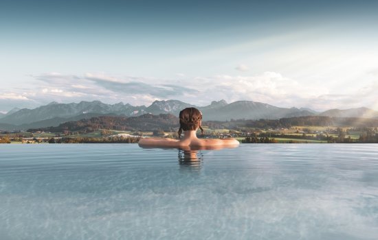 Eine Frau entspannt im Außenpool des Panorama Land- und Wellnesshotels in Rückholz und genießt dabei die wunderschöne Aussicht