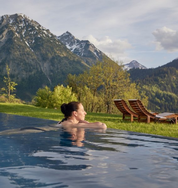Eine Frau genießt eine Auszeit im Außenpool des Hotels Prinz-Luitpold-Bad in Bad Hindelang der eine schönen Panoramablick auf die umliegenden Berge bietet