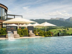 Außenansicht des Hotel Bergkristalls - Mein Resort im Allgäu in Oberstaufen im Sommer mit Blick auf den Außenpool und einen Teil des Hotelgebäudes