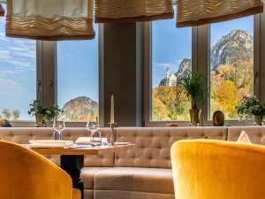 Einblick in das Restaurant des AMERON Neuschwanstein Hotels mit gedeckten Tischen und Ausblick auf Schloss Neuschwanstein im Herbst.