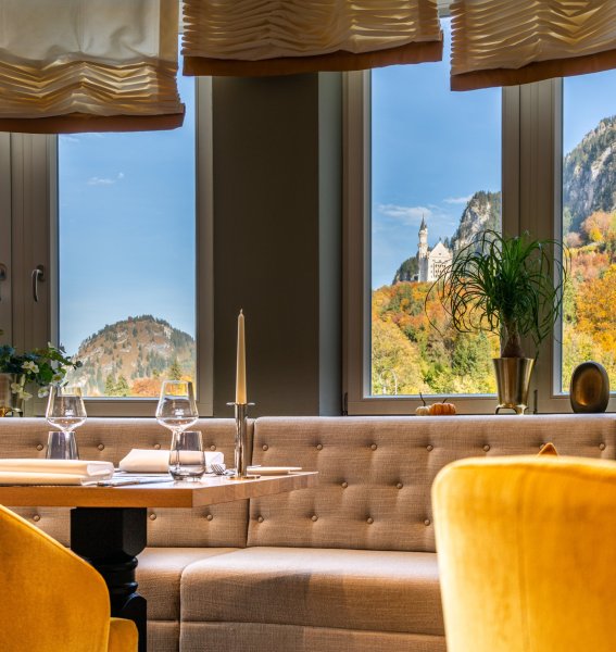 Einblick in das Restaurant des AMERON Neuschwanstein Hotels mit gedeckten Tischen und Ausblick auf Schloss Neuschwanstein im Herbst.