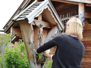 Eine Mitarbeiterin der Alpzitt Chalets in Burgberg dekoriert ein Kruzifix mit Blumen.