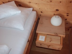 Ein gemütliches Bett mit Nachtkästchen aus Holz im Biohotel Mattlihüs in Bad Hindelang