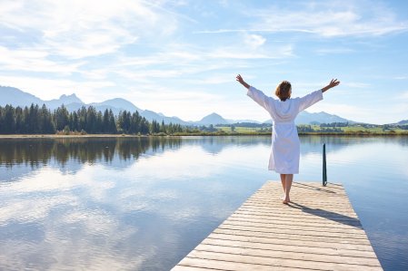 Eine Frau genießt im Bademantel das schöne Wetter auf dem Steeg des Sees in der Nähe des Biohotels Eggensberger in Füssen, Hopfen am See