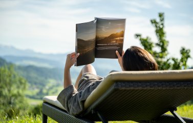Eine Frau liest im Bademantel auf einer Liege im Außenbereich des Hotels Bergkristall - Mein Resort im Allgäu in Oberstaufen eine Zeitschrift und entspannt