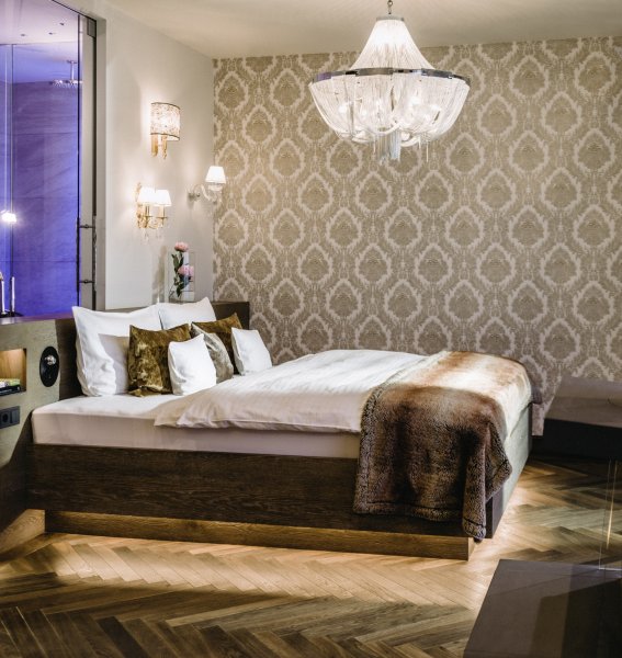 Einblick in eines der gemütlichen und modernen Zimmer im Hotel König Ludwig in Schwangau mit Blick auf ein großes Doppelbett und das Bad im offenen Konzept