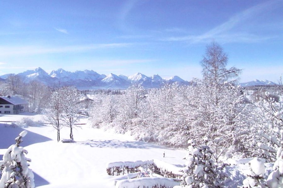 Ausblick vom Hotel Bannwaldsee in Halblech auf den verschneiten Garten und die Berge an einem schönen Wintertag