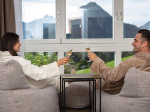 Ein Paar genießt in den Sesseln mit einem Glas Sekt den Ausblick im Kühberg - Das Hotel über Oberstdorf