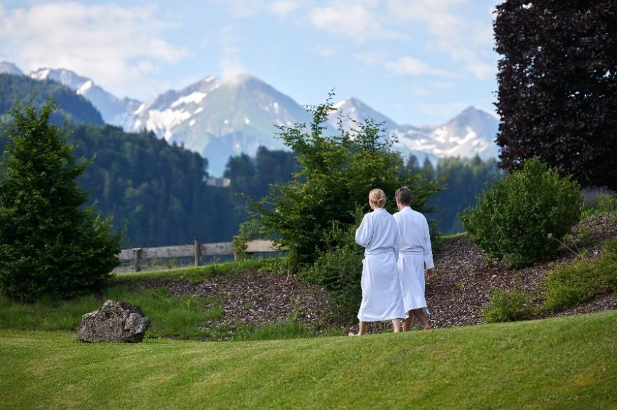 Gäste im SCHÜLE's Gesundheitsresort & SPA in Oberstdorf streifen in Bademänteln durch den großen Garten