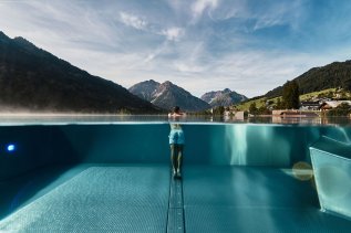 Ein Gast im Travel Charme Ifen Hotel in Kleinwalsertal schwimmt im Außenpool und genießt die Aussicht