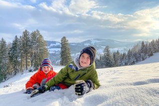 Zwei Kinder spielen im Schnee vor dem MONDI Resort Oberstaufen