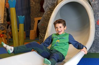 Ein Kind rutscht im Spielzimmer im Mondi Resort Oberstaufen eine Rutsche hinunter