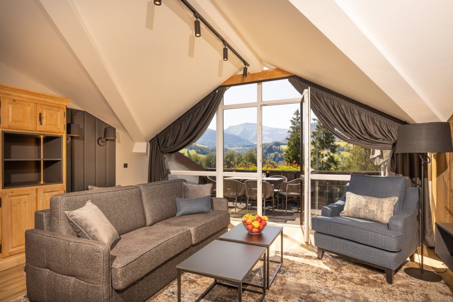 Einblick in eines der Familien Appartements im Mondi Resort in Oberstaufen mit Blick auf ein gemütliches Sofa und den Balkon mit tollem Ausblick